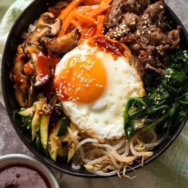 A colorful bowl of traditional Korean Bibimbap with vegetables, rice, and sauce.