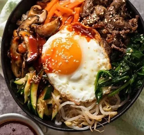 A colorful bowl of traditional Korean Bibimbap with vegetables, rice, and sauce.