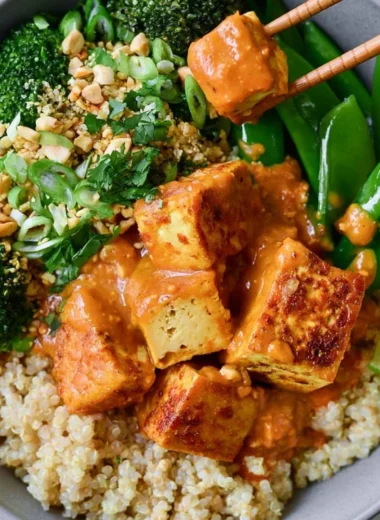 Cozy Thai Peanut Tofu Quinoa Bowl topped with fresh vegetables and peanut sauce