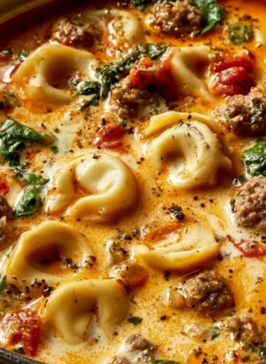 A bowl of Italian Sausage Tortellini Soup with garnishes on a wooden table.