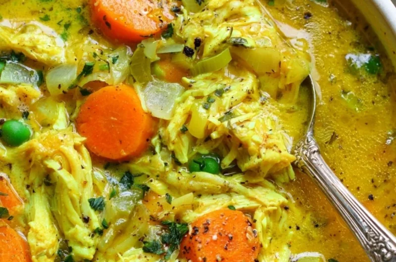 Healthy chicken soup with turmeric and ginger in a bowl, garnished with herbs.