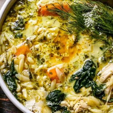 Creamy turmeric lemon chicken and orzo soup garnished with fresh herbs.